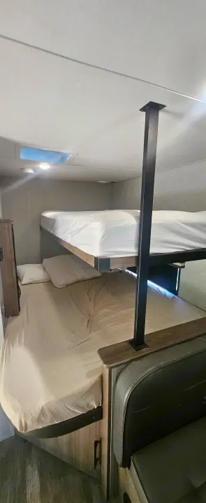 RV rental interior with cozy bunk beds on the left and a dark green dinette bench on the right, providing compact sleeping and seating.. Grand Design Imagine AIM 2023