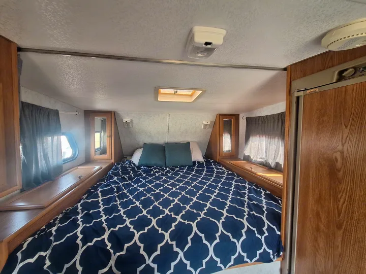 Inviting rv rental bedroom showcasing a bed with patterned bedding, wood cabinets, windows with curtains, and a skylight.. Glacier Campers Truck Camper 2016
