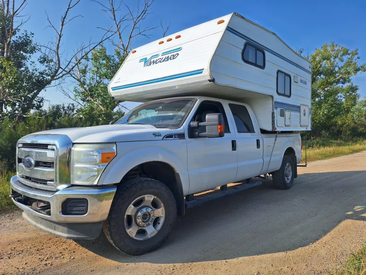 White Ford F-350 truck with a Vanguard truck camper, ideal for an RV rental outdoor adventure on a dirt road.. Glacier Campers Truck Camper 2016