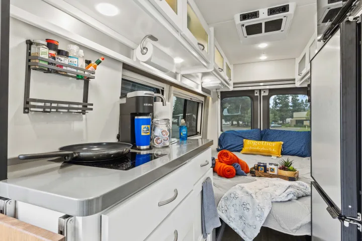 Cozy RV rental interior featuring a compact kitchen with a Keurig & cooktop, plus a comfy bed with a 'together' pillow & paw print blanket.. Coachmen Beyond 2021