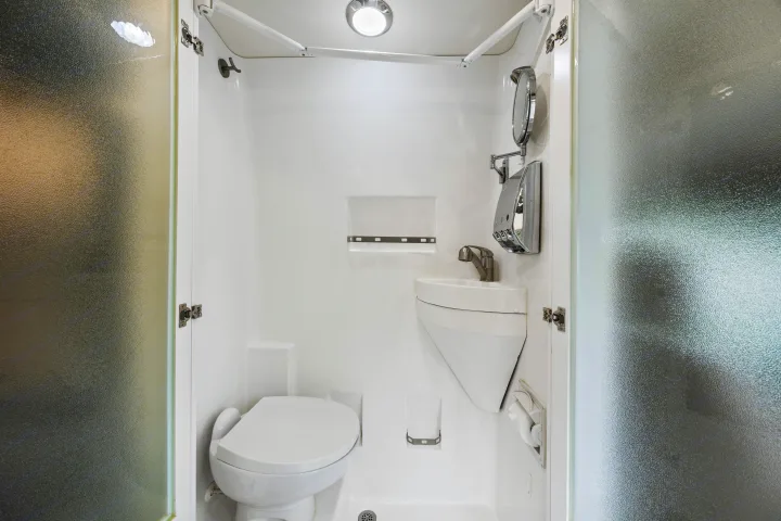 Compact, all-white RV rental bathroom with toilet, corner sink, shower, and mirror, maximizing small space.. Coachmen Beyond 2021