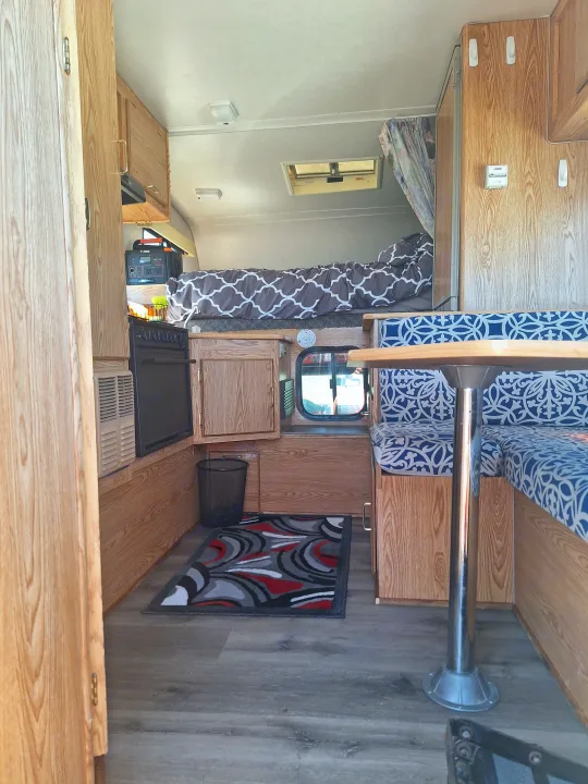 Cozy rv rental interior: bedroom, dinette with blue patterned cushions, and kitchenette with wood cabinetry.. Glacier Campers Truck Camper 2016