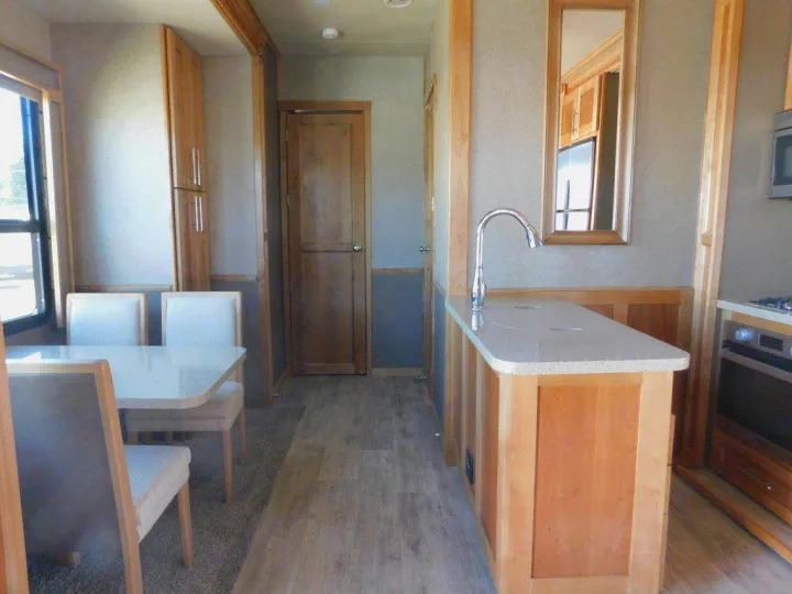 Modern **rv rental** kitchen featuring an island sink, dining area, wood cabinetry, oven, and window. Bright interior.. Vanleigh RV Vilano 2018