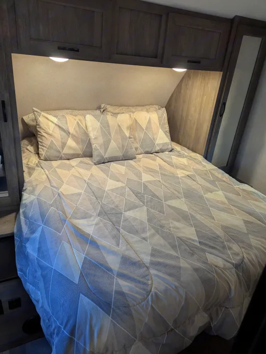 Cozy RV rental bedroom features a comfy bed with modern geometric bedding, overhead storage, and integrated lighting.. Forest River Vibe 2020
