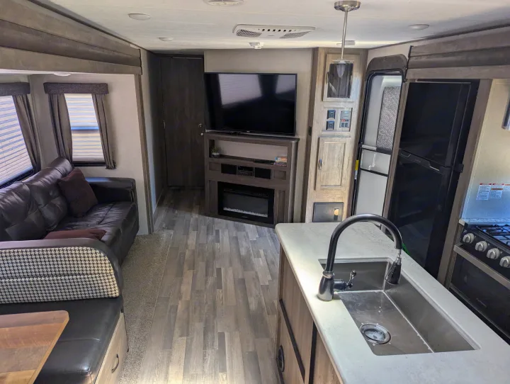 This modern RV rental interior features a spacious living area with a sofa, TV, fireplace, and full kitchen. Bright and clean.. Forest River Vibe 2020