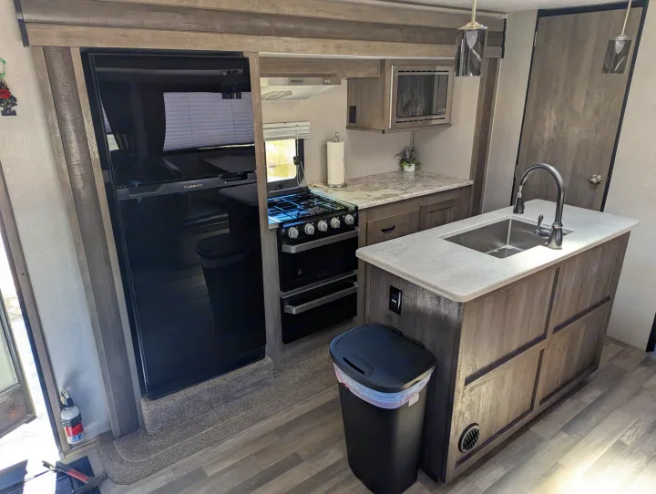 Spacious RV rental kitchen featuring a modern fridge, stove, microwave, and an island sink.. Forest River Vibe 2020