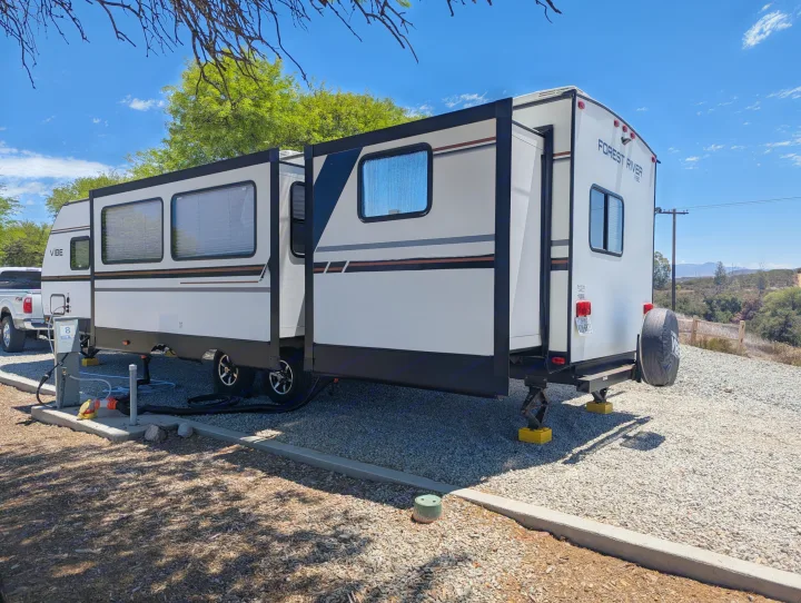 This RV rental, a Forest River Vibe travel trailer, is parked and set up at a sunny campsite with its slide-out extended.. Forest River Vibe 2020