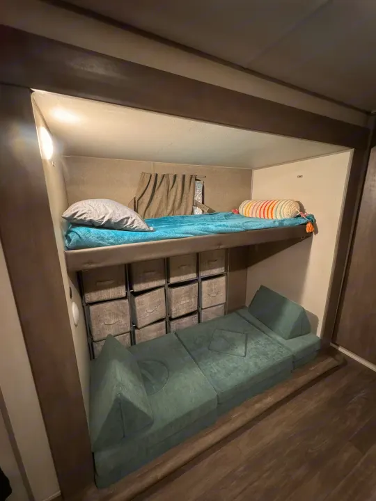 This RV rental features a cozy bunk bed above storage bins and a green modular play couch, maximizing space in a compact interior.. Forest River Aurora Aurora 2024