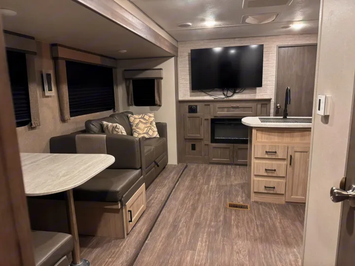 Spacious RV rental living area with a sofa, dining booth, kitchen, TV, and electric fireplace, perfect for travel.. Forest River Aurora Aurora 2024