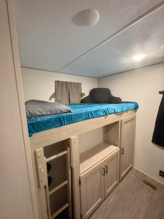 RV rental: A cozy bunk bed sleeping area with a blue blanket, gray pillow, and ample storage cabinets below. Ladder access.. Forest River Aurora Aurora 2024