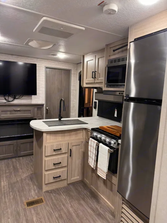 Bright RV rental interior: modern kitchen with stainless appliances, island sink, TV, and fireplace area.. Forest River Aurora Aurora 2024
