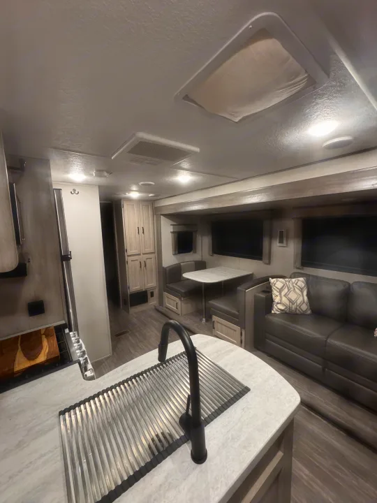 An RV rental interior with a kitchen counter, sink, dining area, sofa, and light wood cabinetry, showcasing a cozy living space.. Forest River Aurora Aurora 2024