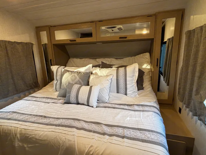 Cozy RV rental bedroom featuring a neatly made bed with white & gray pillows, and overhead storage.. Forest River Wildwood Heritage Glen 2024