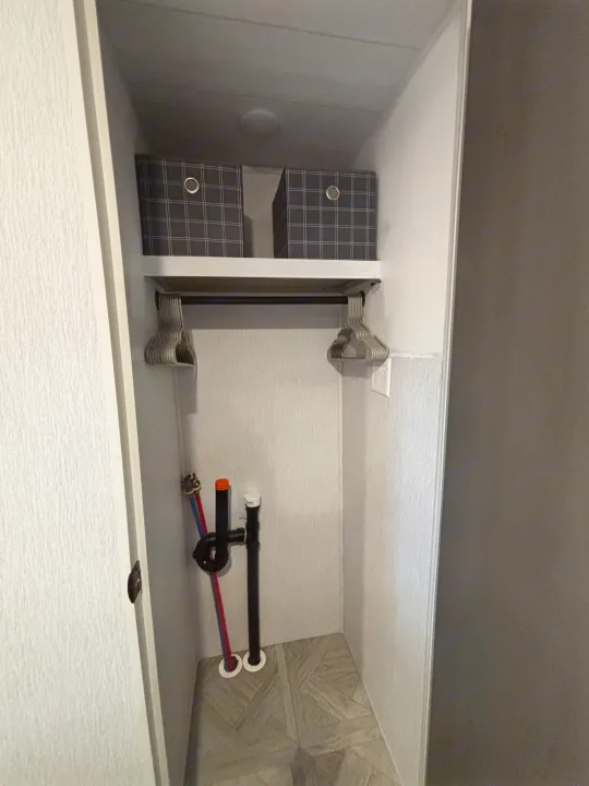 This RV rental utility closet features washer/dryer hookups, a shelf with storage bins, and a hanging rod with hangers.. Forest River Wildwood Heritage Glen 2024