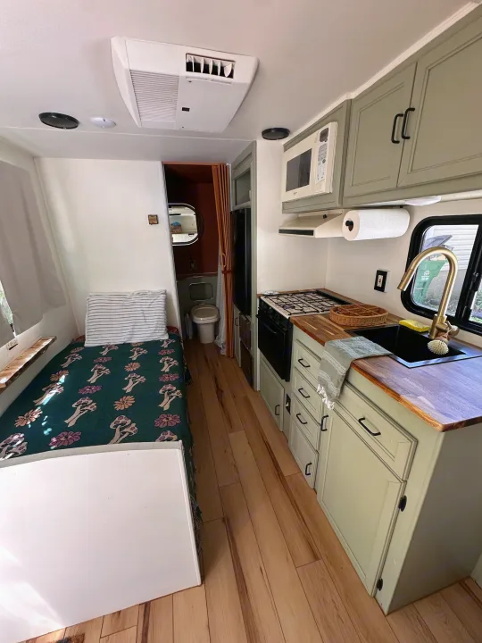Bright rv rental interior featuring a compact kitchen with green cabinets & wood counters, a bed, and a small bathroom.. Coachmen Catalina 1994