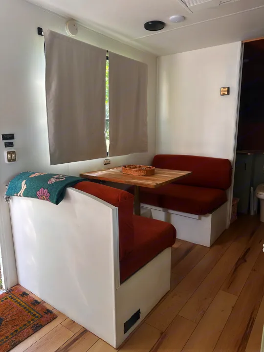 Cozy rv rental dinette interior featuring a wooden table, rust-colored benches, wood floor, and light curtains.. Coachmen Catalina 1994