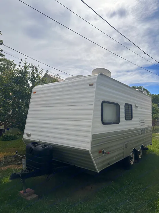 White and green travel trailer RV rental, parked on a grassy lawn under power lines, ready for adventure.. Coachmen Catalina 1994