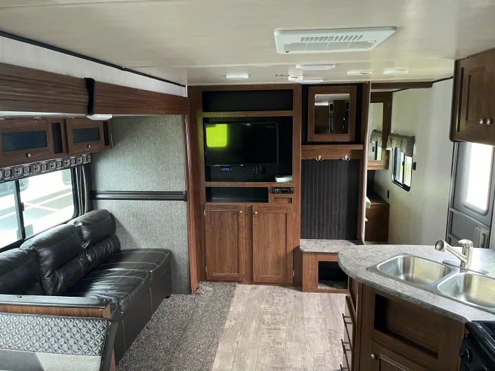 Spacious RV rental interior with a cozy living area, including a sofa, entertainment center, and kitchen. Perfect for your next adventure!. Pioneer Bunkhouse 2019