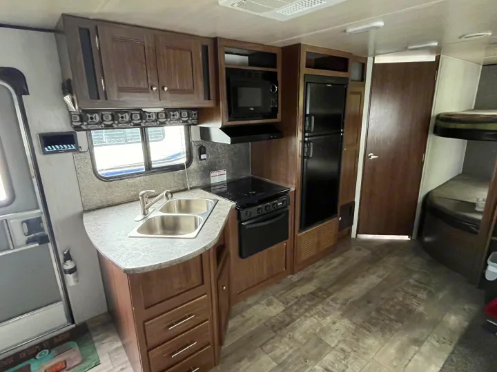 RV rental interior: a functional kitchen area with a double sink, stove, microwave, refrigerator, and rear bunk beds.. Pioneer Bunkhouse 2019