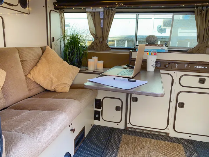 Cozy Westfalia RV rental interior features a laptop workspace, comfy sofa, and window with curtains and fairy lights.. Volkswagen T3 Westfalia 1985