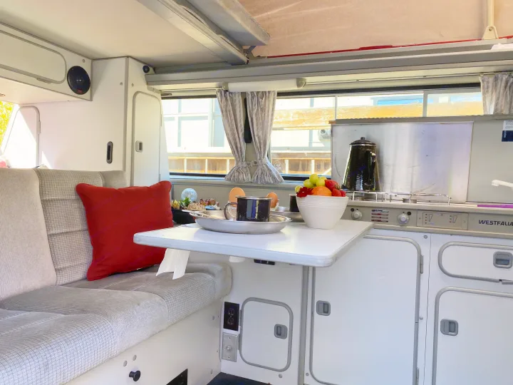 Inside a Westfalia camper van RV rental: a compact kitchen, cozy bench seating, and a table set for breakfast.. Volkswagen Westfalia 1986