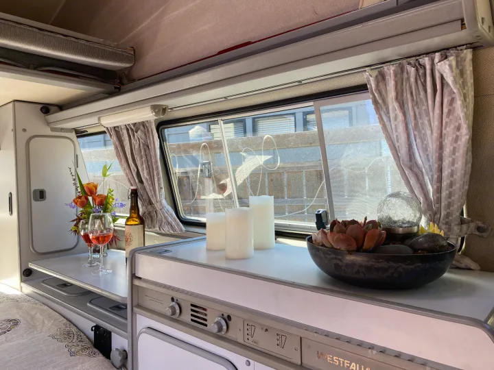 Cozy rv rental Westfalia interior: kitchen counter with wine, flowers, candles, and succulents by the window.. Volkswagen Westfalia 1986