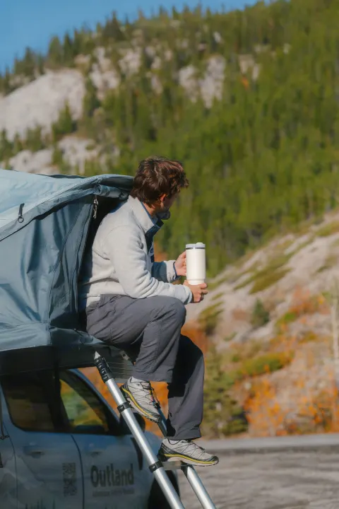Enjoying the view from an Outland RV rental rooftop tent. Perfect for camping adventures with a hot drink.. Ford Maverick 2025