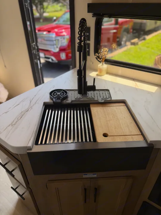 This modern RV rental kitchen features a black sink, integrated drying rack, and wooden cutting board.. Forest River Grey wolf 2026