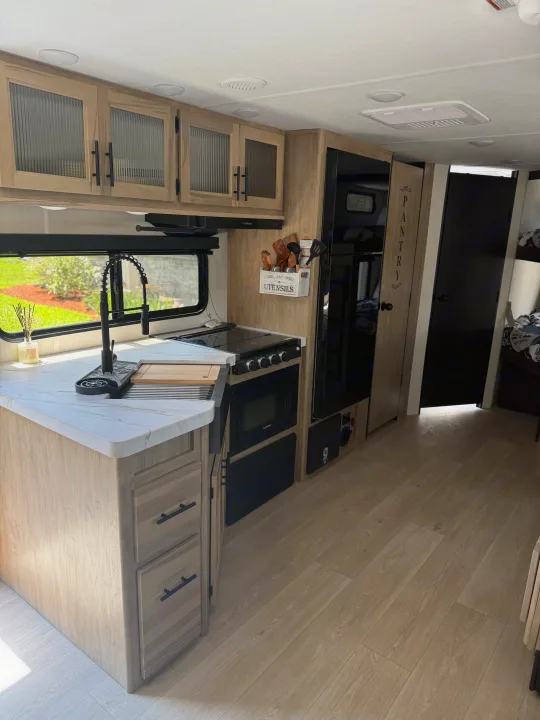 Explore this stylish RV rental kitchen featuring light wood cabinets, white countertops, modern black faucet, and compact appliances.. Forest River Grey wolf 2026