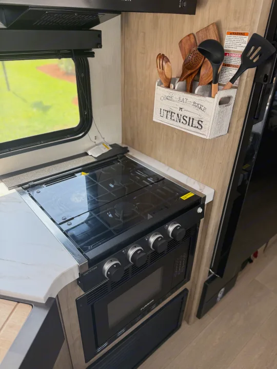 Functional RV rental kitchen: Greystone gas stovetop, Furrion oven/microwave, marble counter, and cooking utensils.. Forest River Grey wolf 2026