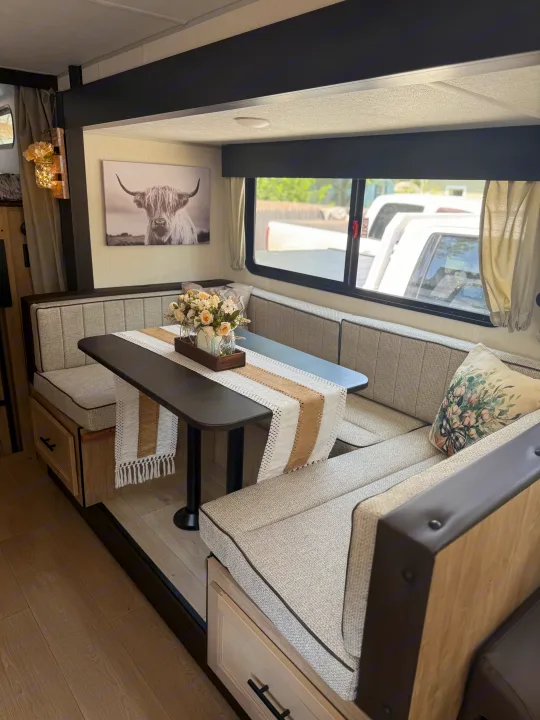 Comfortable RV rental dinette featuring booth seating, a decorative table centerpiece, and Highland cow wall art.. Forest River Grey wolf 2026