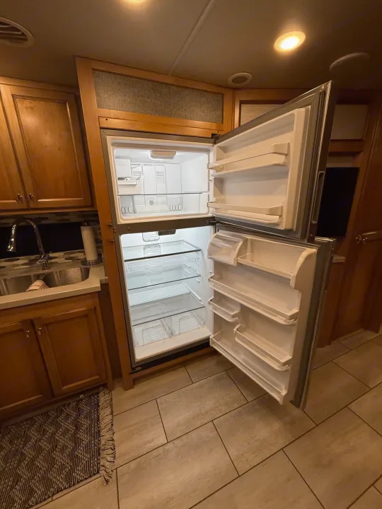 Clean, empty refrigerator in an RV rental kitchen, showcasing spacious interior, sink, and cabinets, ready for your trip.. Tiffin Allegro 2020
