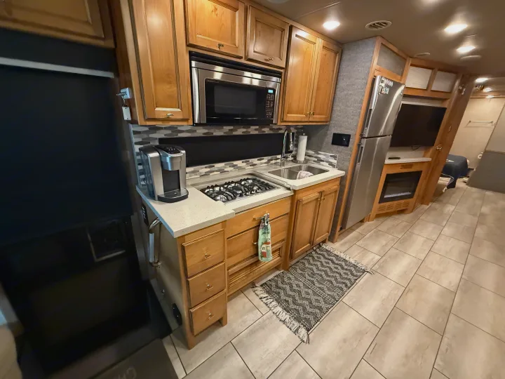 Compact rv rental kitchen with wood cabinets, stainless steel appliances, stove, sink, and coffee maker on a tiled floor.. Tiffin Allegro 2020