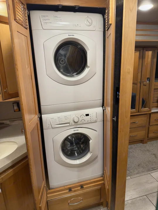 A white Splendide stacked washer and dryer in an open wooden cabinet, perfect for laundry convenience in an RV rental.. Tiffin Allegro 2020