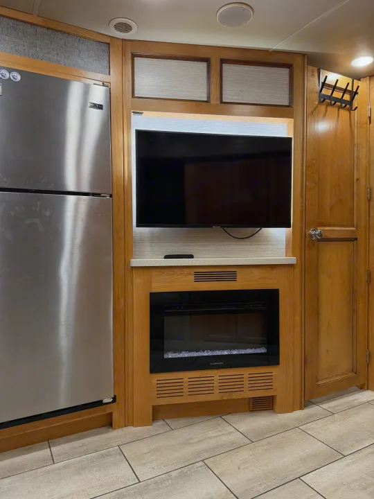 RV rental interior featuring a stainless steel refrigerator, modern TV, and electric fireplace for comfortable living.. Tiffin Allegro 2020