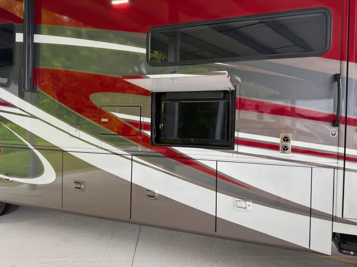 A red, white, and gray rv rental's side, featuring an open compartment with an outdoor TV for prime entertainment.. Tiffin Allegro 2020