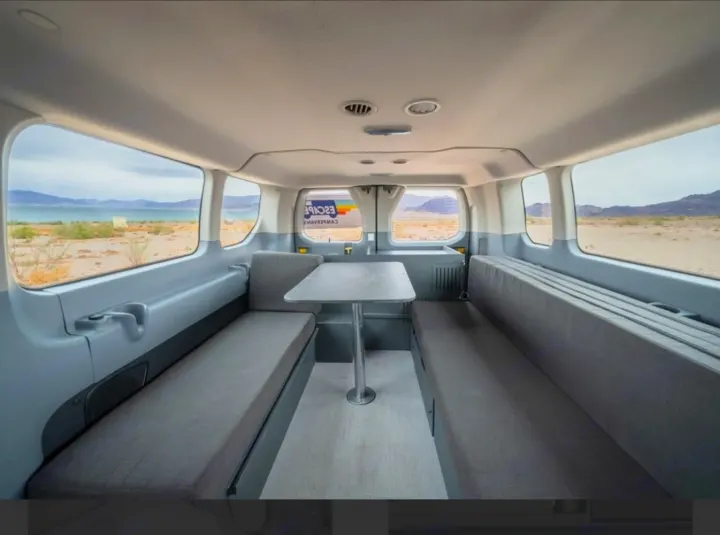 This rv rental campervan interior features a dining table between two bench seats, with a scenic lake and desert view outside.. Ford Transit 2017