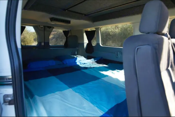 Cozy RV rental interior: A blue-themed bed fills the rear, visible from the side door, with natural light through windows.. Ford Transit 2017