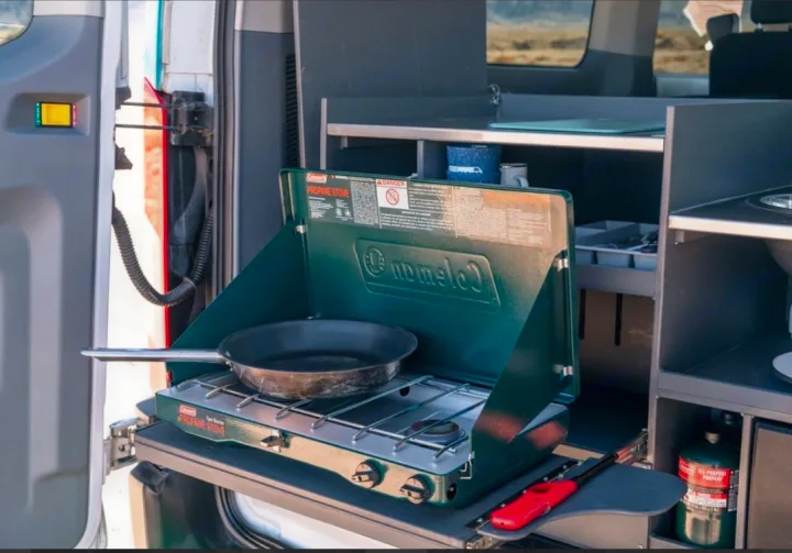 Cooking in an RV rental: a Coleman propane stove with a frying pan ready on a pull-out kitchen unit.. Ford Transit 2017