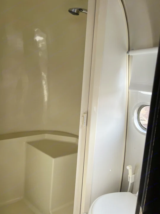 Inside an RV rental: a compact bathroom featuring a shower stall, toilet with bidet, and a small porthole window.. Airstream Bambi International 2006