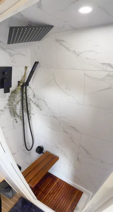 Modern RV rental shower with marble-look tiles, sleek black fixtures, a wood bench, and eucalyptus for a spa feel.. Mercedes Sprinter 2022