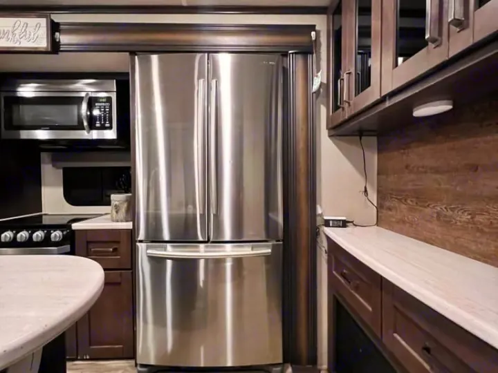 Spacious RV rental kitchen with stainless steel fridge, microwave, dark cabinets & white countertops.. Grand Design Reflection 2020