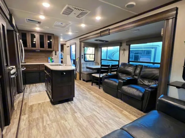 This modern RV rental features a full kitchen with dark cabinets and an island, leading to a living area with black recliners.. Grand Design Reflection 2020