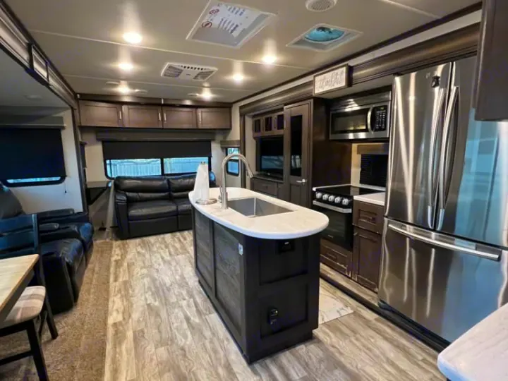 Spacious rv rental interior: modern kitchen with island, stainless steel appliances, and black leather living room.. Grand Design Reflection 2020