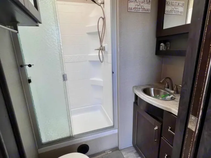An RV rental bathroom, showing a white shower stall with a sliding glass door and a dark wood vanity with a sink.. Grand Design Reflection 2020