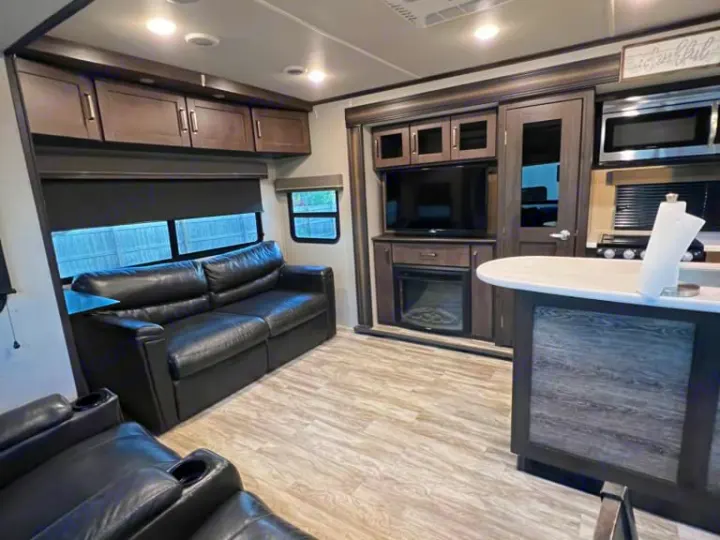 Spacious rv rental interior featuring a modern living room with leather sofas, TV, fireplace, and well-equipped kitchen.. Grand Design Reflection 2020