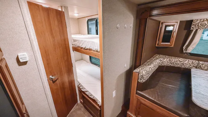 Cozy RV rental interior: bunk beds, a dinette with patterned cushions, and a thermostat. Great for trips!. Coachmen Apex 2016