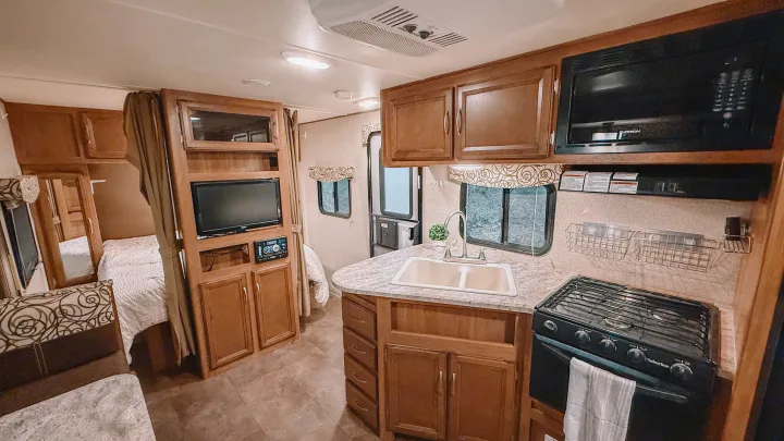 Cozy RV rental interior featuring a kitchen with stove, sink, microwave, TV, and a bedroom area with a bed.. Coachmen Apex 2016