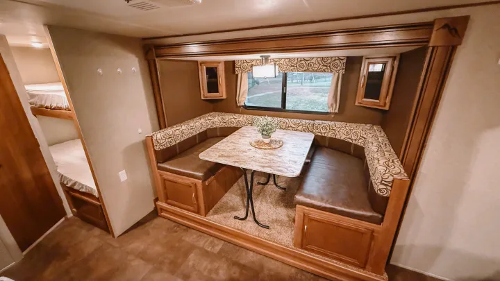 Spacious RV rental dinette area with comfortable U-shaped seating, a table, and bunk beds visible for extra guests.. Coachmen Apex 2016