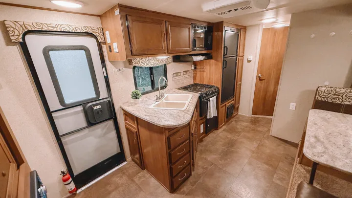 RV rental interior: A well-appointed kitchen with wooden cabinets, sink, stove, microwave, fridge, and an entry door.. Coachmen Apex 2016